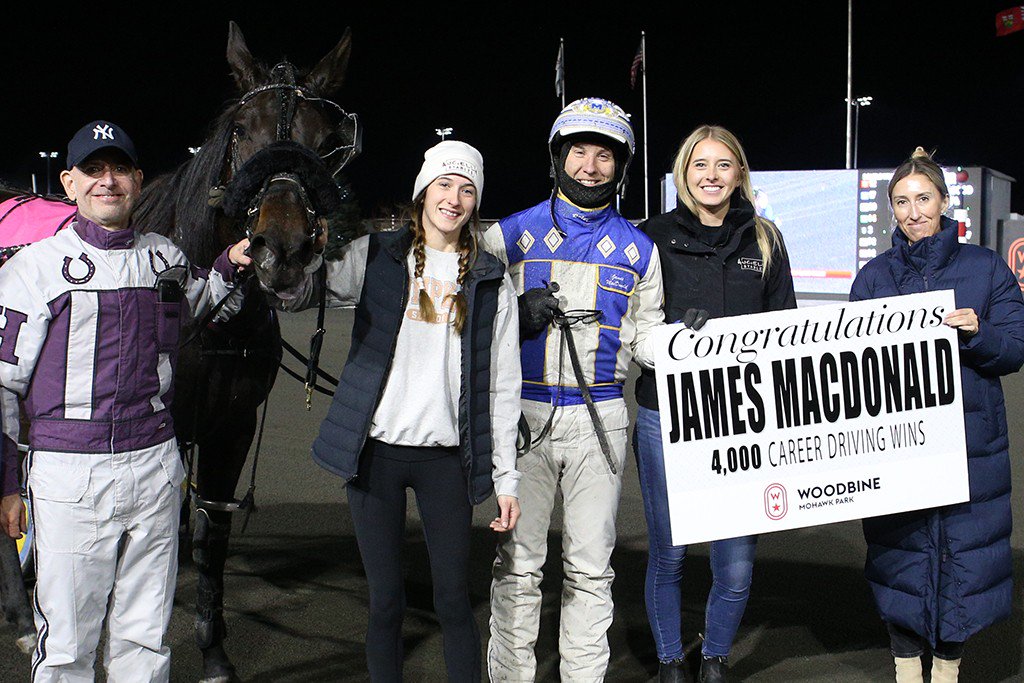 James MacDonald, joined by his wife Paige MacDonald, is presented with a sign to recognize his 4,000th win from Megan Walker, Senior Manager of Standardbred Racing.